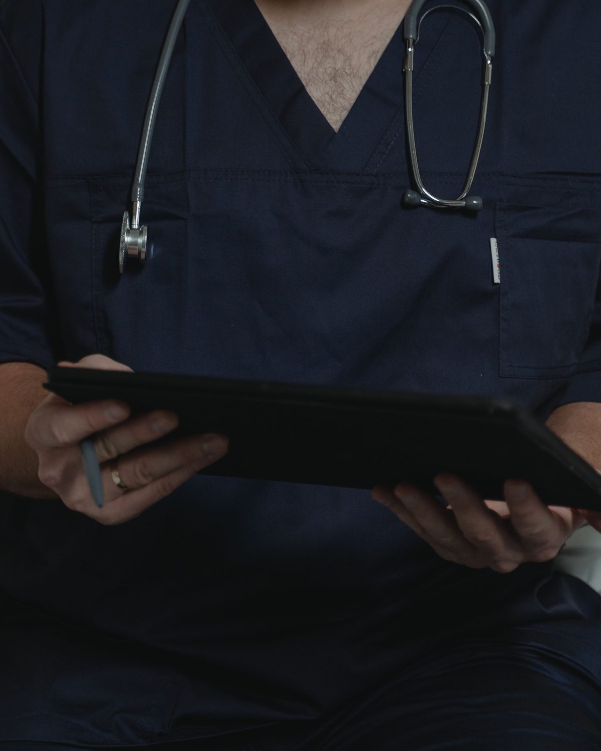 Doctor in navy scrubs with a stethoscope, holding a tablet