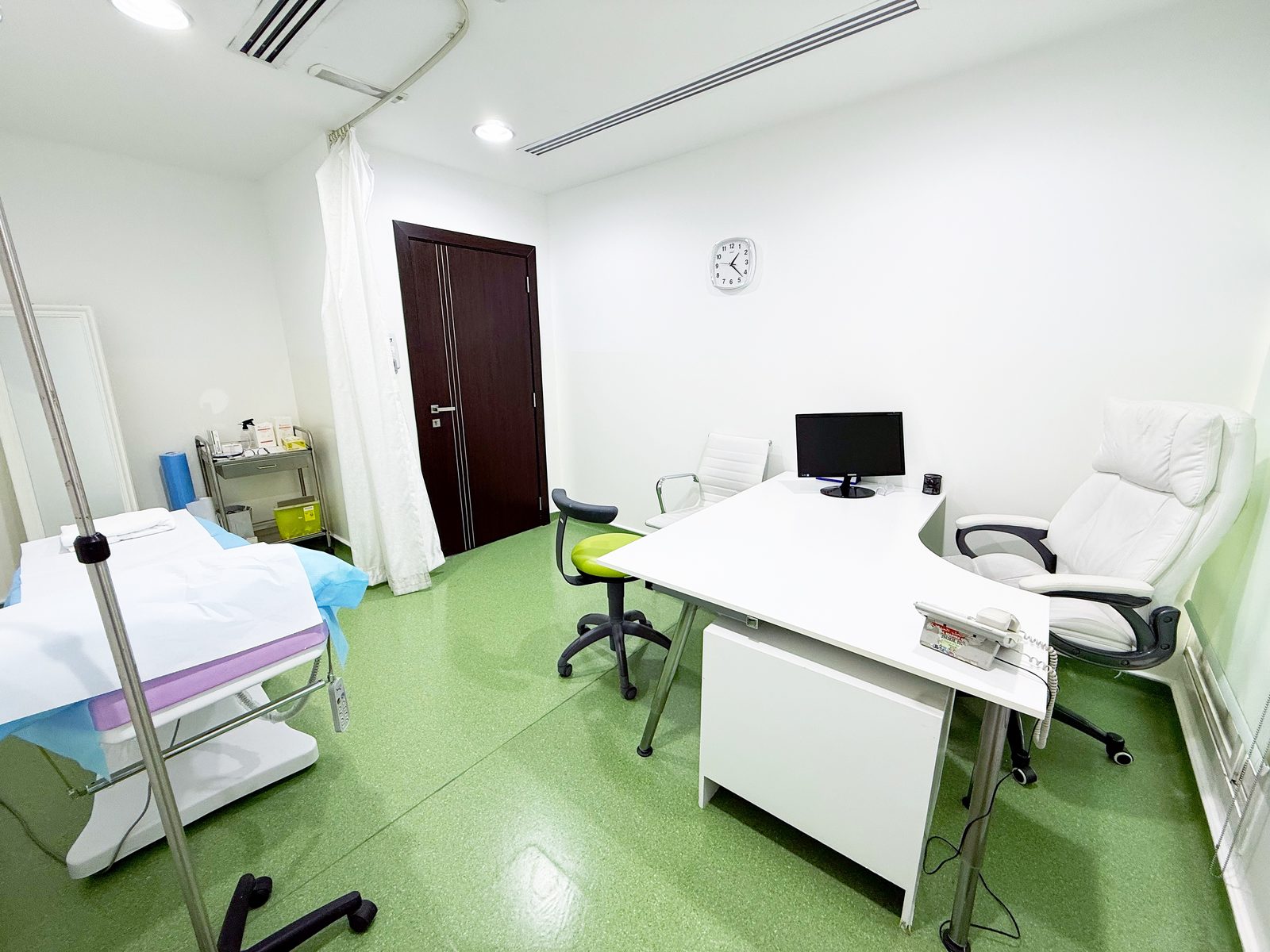 Consultation room with doctor's desk and examination bed in a poly clinic in Jumeirah, Dubai
